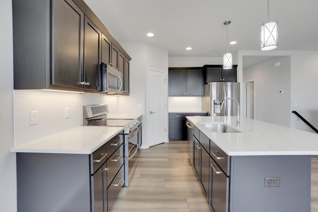 kitchen with backsplash, a sink, light wood-style floors, pendant lighting, and appliances with stainless steel finishes