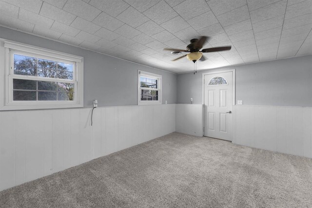carpeted spare room featuring a ceiling fan, a wainscoted wall, and wood walls