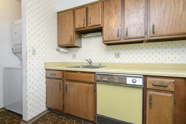 kitchen featuring white dishwasher, light countertops, stacked washer / dryer, and a sink