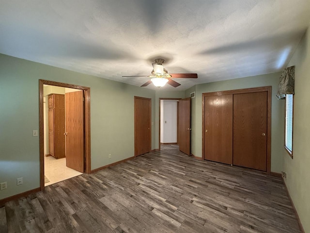 unfurnished bedroom featuring ceiling fan, multiple closets, baseboards, and wood finished floors