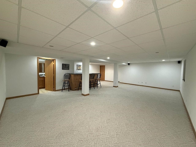 finished below grade area with bar, baseboards, carpet floors, and a paneled ceiling