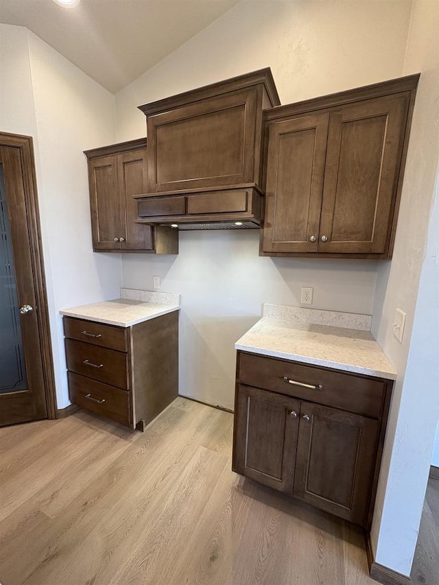 1354 Shelby Ln, De Pere, WI 54115 - kitchen with light wood-style floors, light countertops, dark brown cabinetry, custom range hood, and lofted ceiling