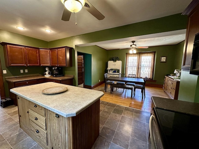 kitchen with electric range oven, light countertops, a center island, a ceiling fan, and baseboards