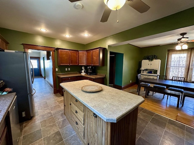 kitchen featuring light countertops, a center island, freestanding refrigerator, a ceiling fan, and baseboards