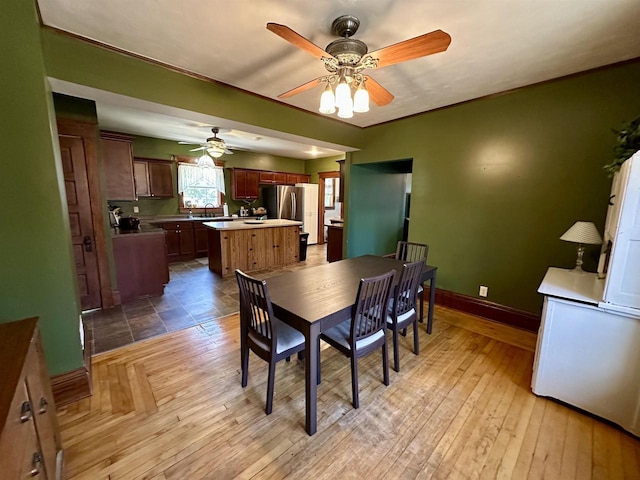 dining space with baseboards, a ceiling fan, and light wood finished floors