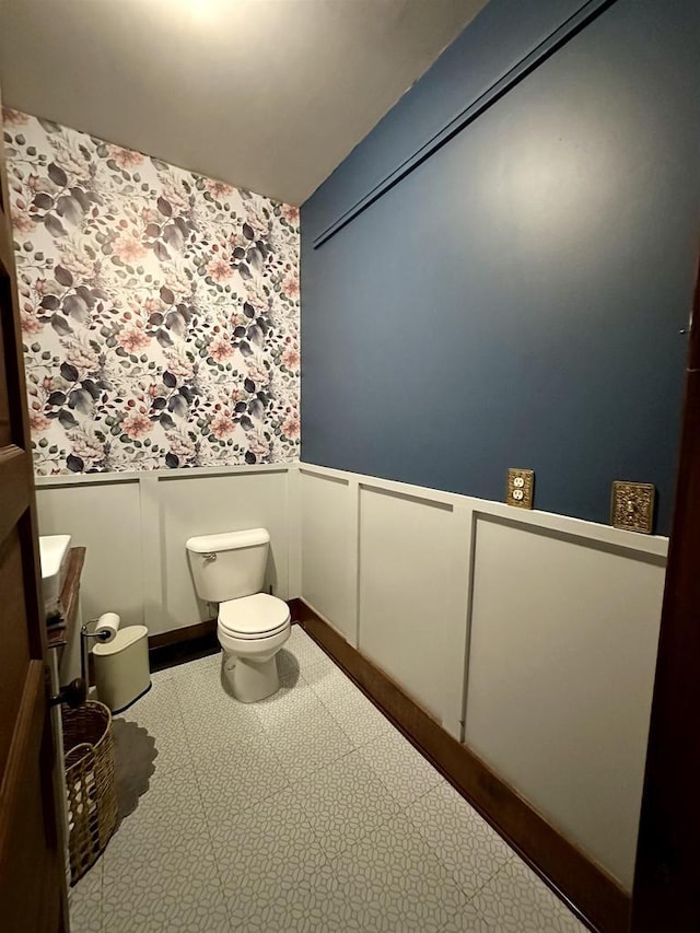 half bath with vanity, a wainscoted wall, toilet, a decorative wall, and wallpapered walls