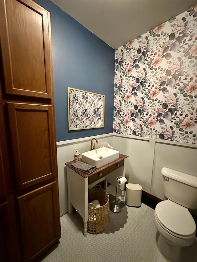 half bathroom featuring a sink, wallpapered walls, wainscoting, and toilet