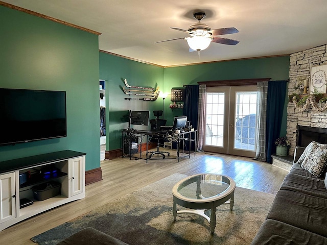 living area featuring a stone fireplace, a ceiling fan, wood finished floors, and ornamental molding