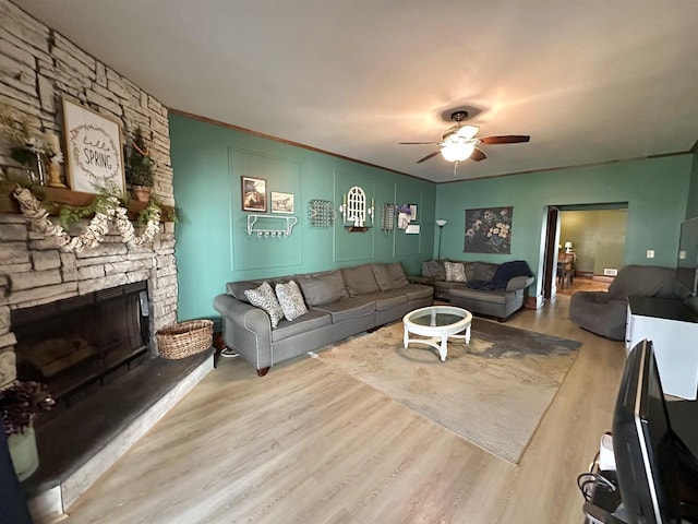 living room featuring a stone fireplace, a ceiling fan, wood finished floors, and ornamental molding