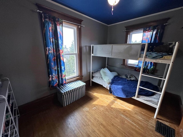 bedroom with wood-type flooring, visible vents, and ornamental molding