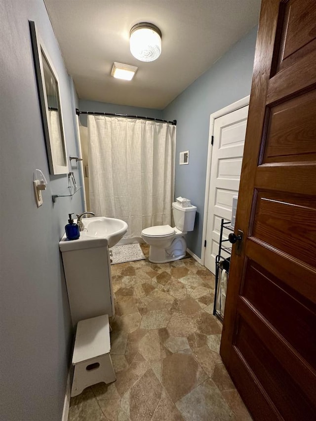 bathroom with vanity, curtained shower, toilet, baseboards, and stone finish floor