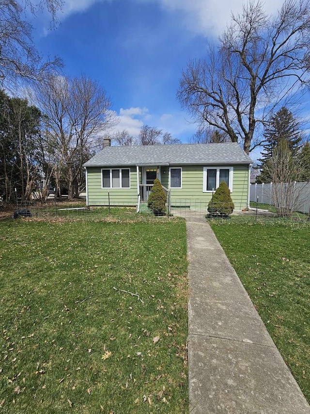 view of front facade with roof with shingles, a chimney, a front yard, and fence