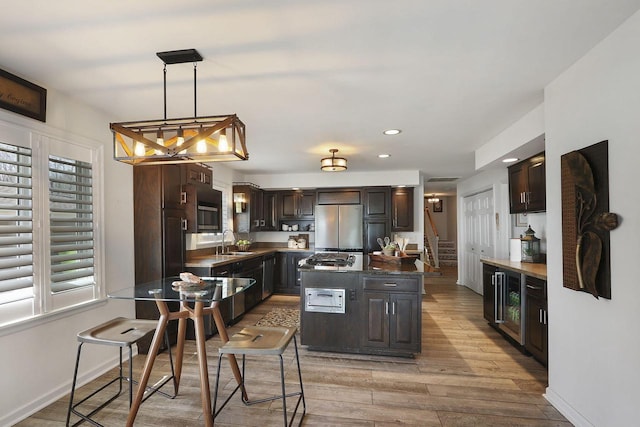 kitchen featuring light wood-style flooring, a center island, a sink, dark brown cabinets, and freestanding refrigerator