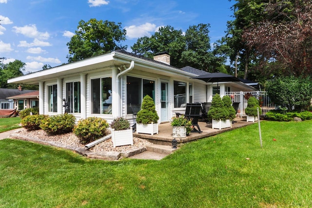 rear view of property with a chimney, a patio area, and a lawn