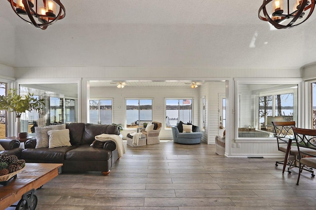 living room with ceiling fan with notable chandelier, hardwood / wood-style flooring, a textured ceiling, and a water view