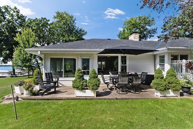 back of property with a shingled roof, a chimney, a yard, and a patio