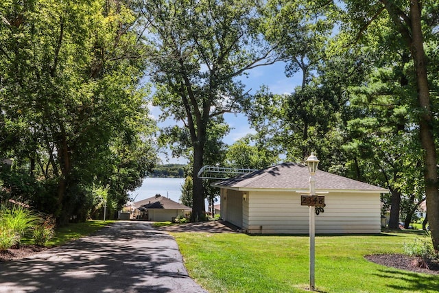 view of side of property featuring a yard, driveway, a water view, and roof with shingles