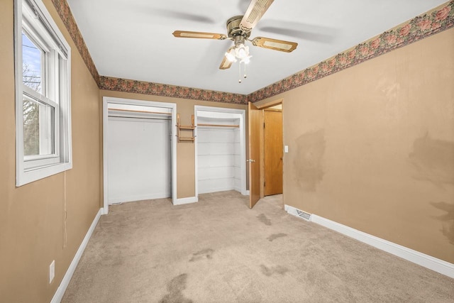 unfurnished bedroom featuring baseboards, multiple closets, light colored carpet, and ceiling fan