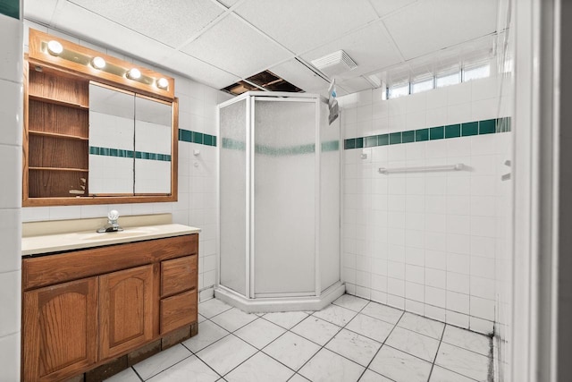 full bathroom featuring tile walls, vanity, a stall shower, and visible vents