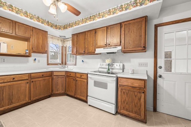 kitchen with brown cabinets, under cabinet range hood, light countertops, a ceiling fan, and white range with electric cooktop