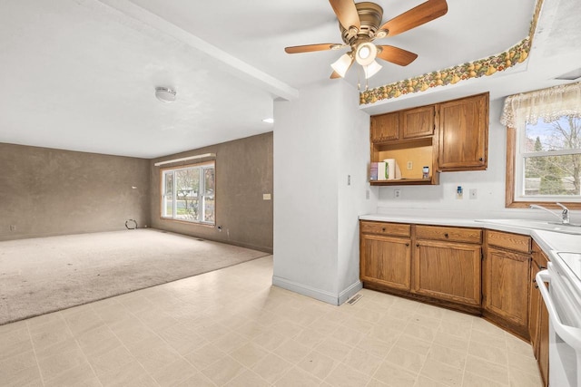 kitchen featuring stove, brown cabinetry, light carpet, and a sink