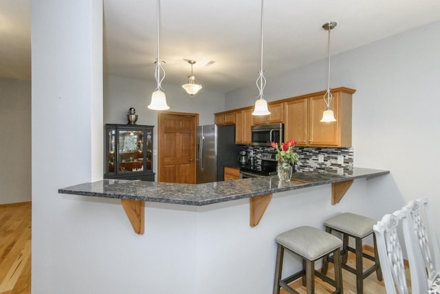 kitchen with stainless steel appliances, a peninsula, light wood-style flooring, and tasteful backsplash