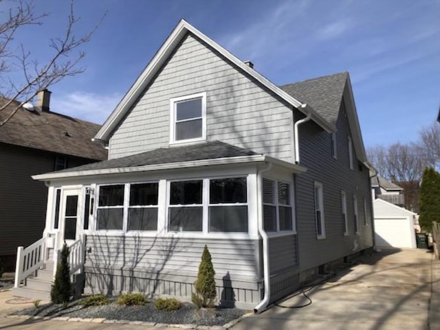 exterior space with a detached garage, an outdoor structure, and roof with shingles