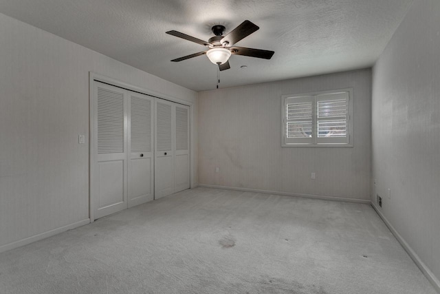 unfurnished bedroom with carpet flooring, a textured ceiling, baseboards, a closet, and ceiling fan