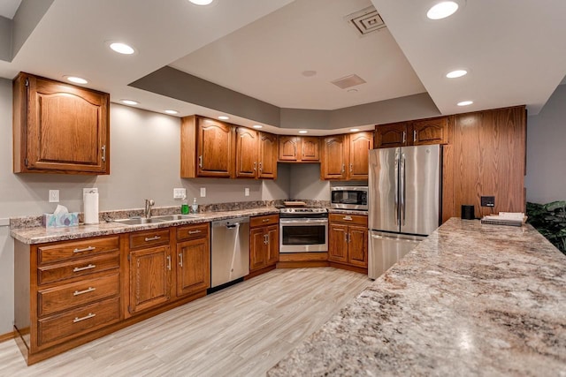 kitchen with a sink, brown cabinets, light wood-type flooring, stainless steel appliances, and recessed lighting