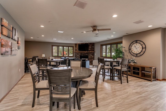dining space with light wood finished floors, a ceiling fan, a brick fireplace, and a wealth of natural light