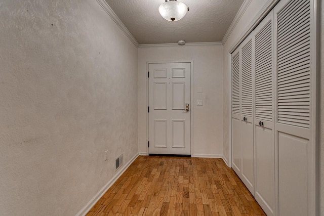 hallway with a textured ceiling, light wood-type flooring, baseboards, visible vents, and ornamental molding