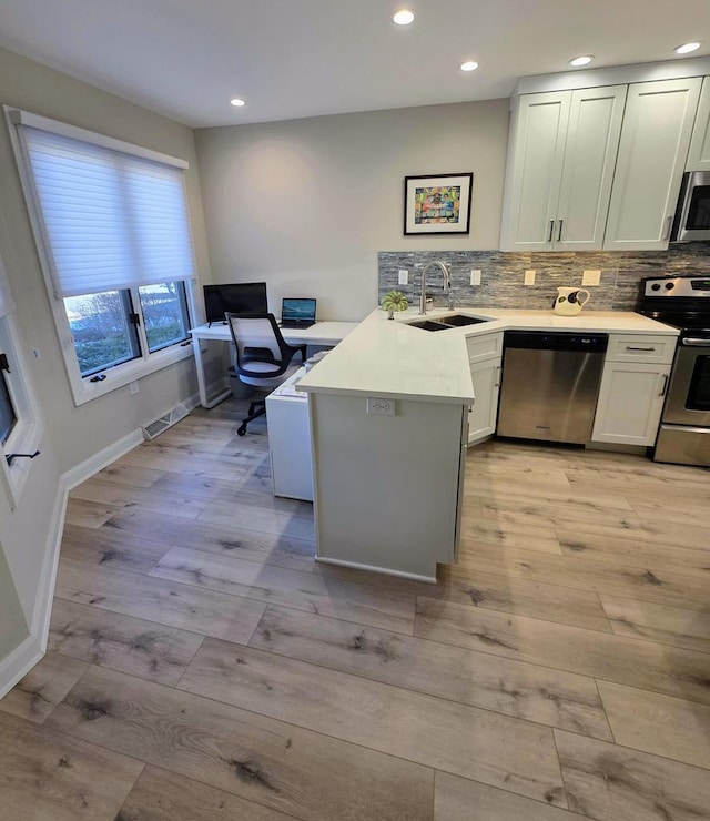 kitchen with a peninsula, light wood-type flooring, stainless steel appliances, and a sink