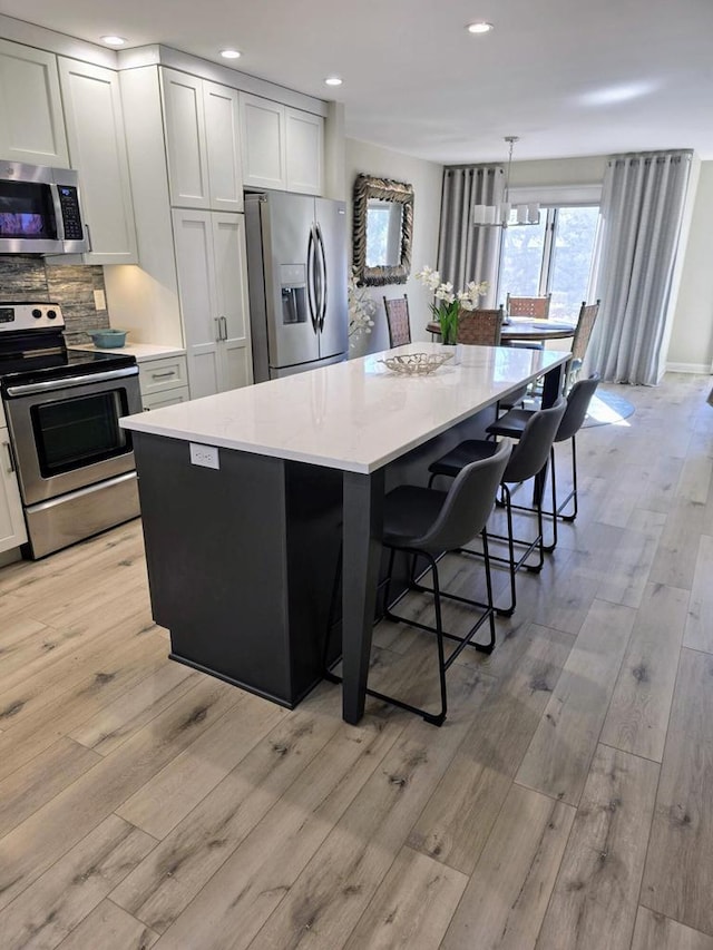 kitchen with stainless steel appliances, a center island, a kitchen breakfast bar, tasteful backsplash, and light wood-style floors