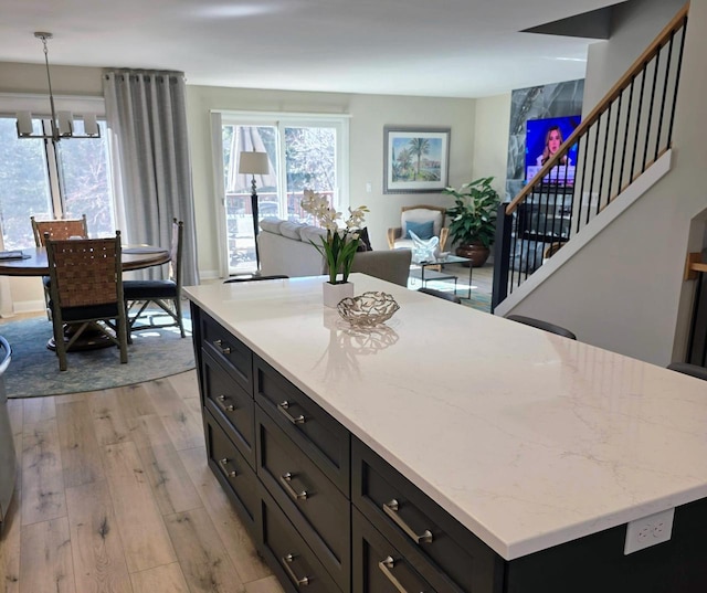 kitchen with light stone counters, plenty of natural light, light wood finished floors, and dark cabinetry