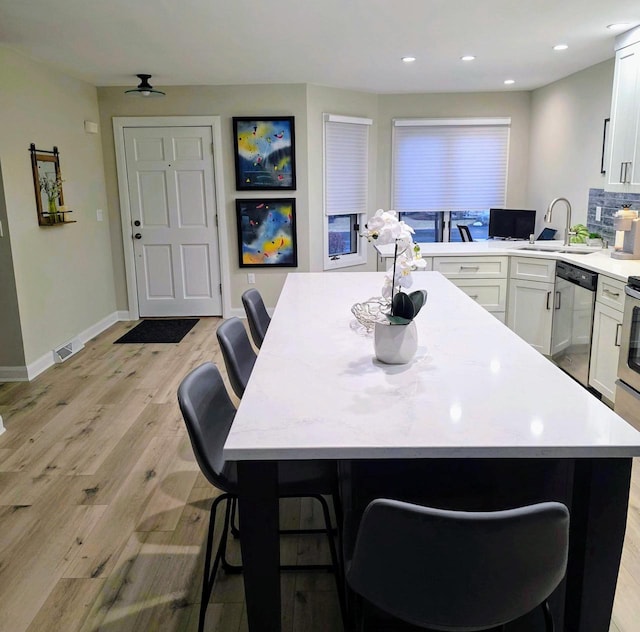 kitchen with white cabinets, light countertops, a sink, light wood-type flooring, and dishwasher