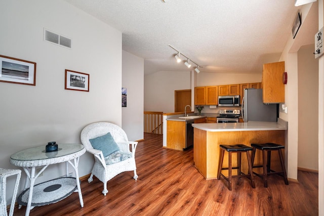 kitchen featuring brown cabinets, a sink, visible vents, stainless steel appliances, and a peninsula