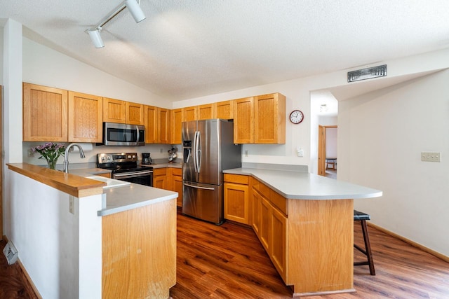 kitchen featuring stainless steel appliances, a kitchen bar, rail lighting, dark wood-type flooring, and a peninsula