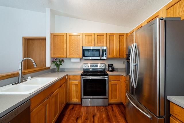 kitchen featuring appliances with stainless steel finishes, brown cabinets, dark wood-style flooring, a sink, and lofted ceiling