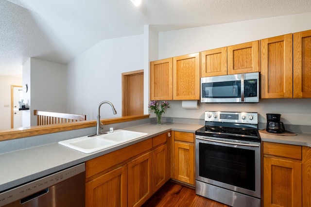 kitchen with a sink, stainless steel appliances, dark wood-type flooring, vaulted ceiling, and light countertops