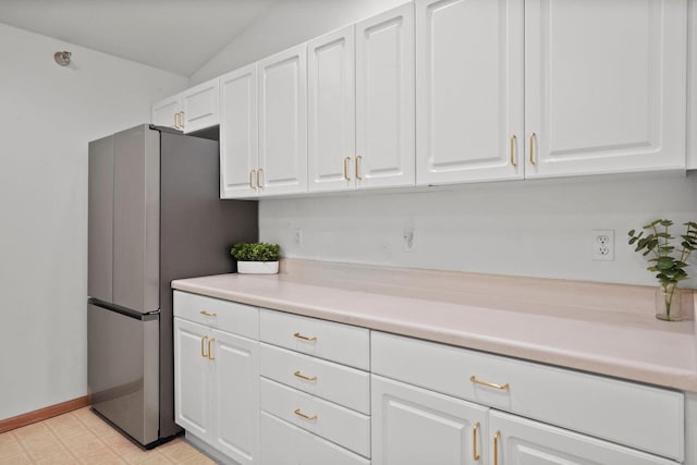 kitchen featuring white cabinets, lofted ceiling, light floors, light countertops, and freestanding refrigerator