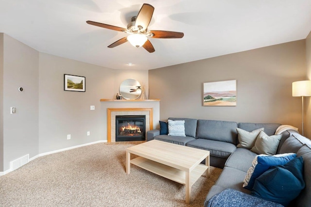 carpeted living room featuring baseboards, a tiled fireplace, visible vents, and ceiling fan