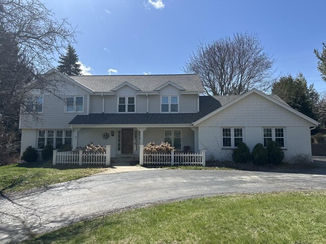 traditional home featuring a shingled roof, driveway, covered porch, and a front yard
