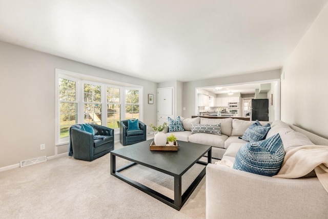 living area with baseboards, visible vents, and light carpet