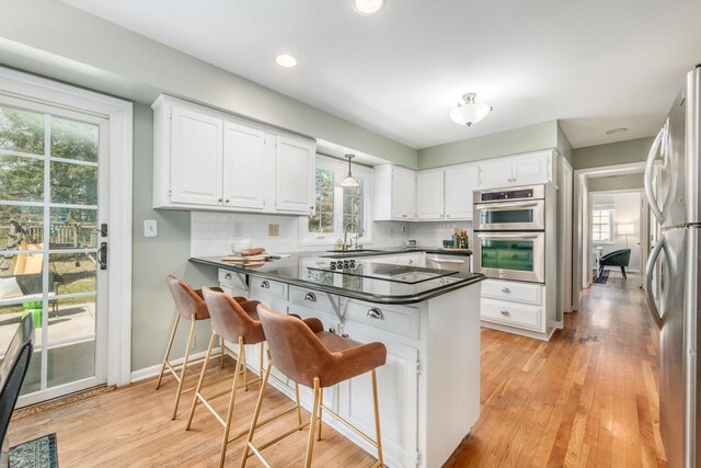 kitchen with stainless steel appliances, dark countertops, a sink, a peninsula, and white cabinetry