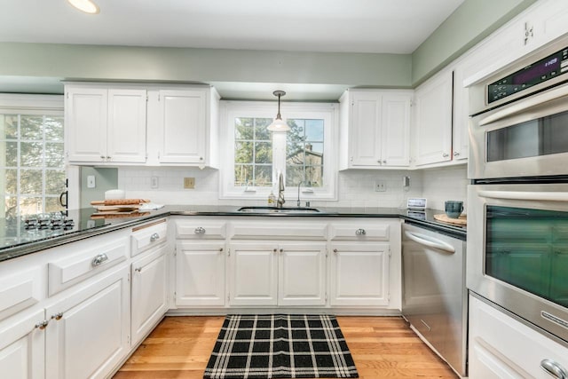 kitchen with backsplash, dark countertops, a sink, appliances with stainless steel finishes, and white cabinetry