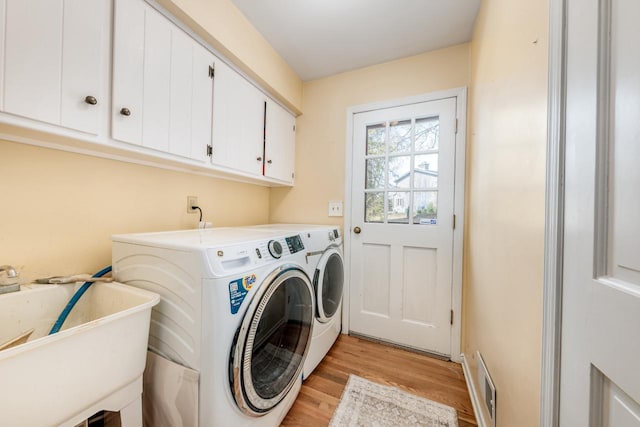 laundry room with a sink, cabinet space, light wood finished floors, washing machine and dryer, and visible vents