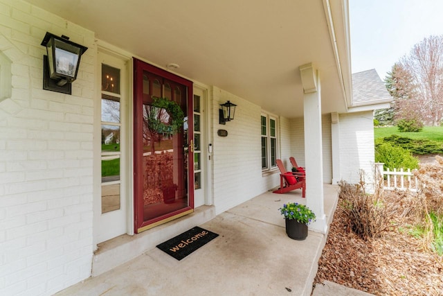 property entrance featuring a porch, brick siding, and roof with shingles