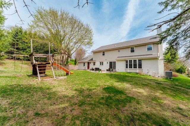 rear view of property with a patio area, a playground, central air condition unit, a chimney, and a yard