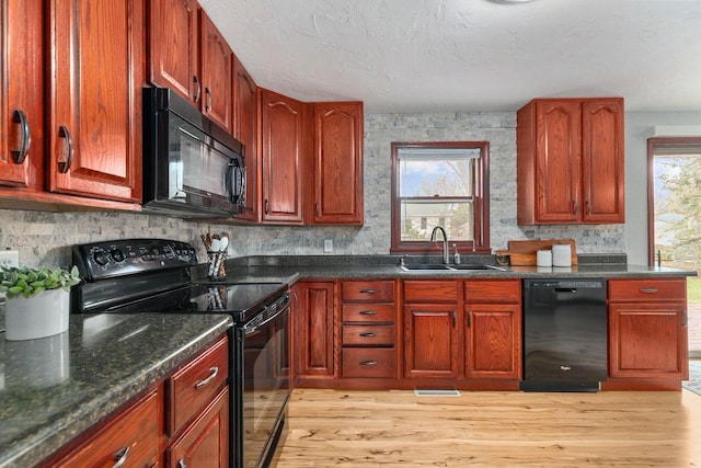 kitchen with a sink, a textured ceiling, dark stone counters, light wood-type flooring, and black appliances
