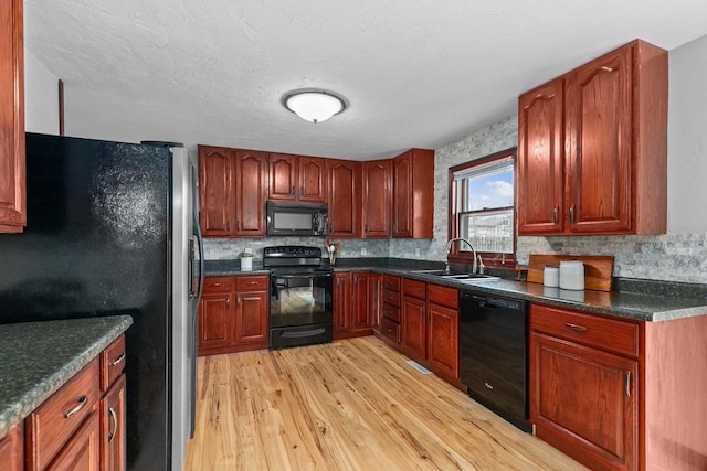 kitchen with black appliances, dark countertops, a sink, and light wood-style floors